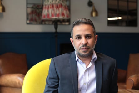A middle-aged Arab man in a suit sits in a yellow chair, posing for a photograph