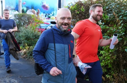 Two men smile at the camera as they walk past, while another man follows behind holding his jacket