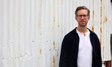 Matt Lloyd-Rose photographed in Cyprus, in front of a white corrugated iron fence, April 2023