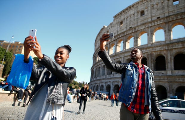 Tourists take selfies in front of the Colosseum in Rome