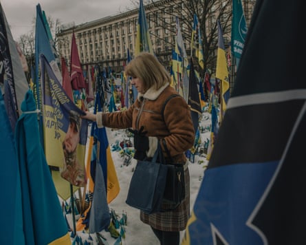 A woman looks at a face on a flag amid many Ukrainian flags in the snow-covered square.