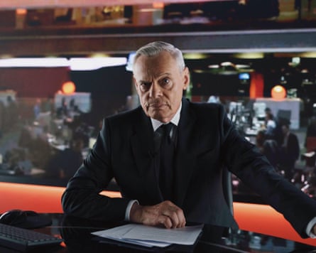 Martin Clunes as Huw Edwards sits at a news desk, frowning at the camera.