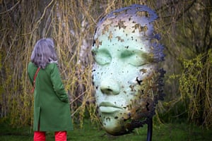 Woman in dark green coat looking at enormous sculptured face outdoors