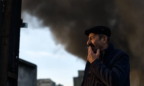 A warehouse guard is smoking a cigarette after rocket attacks on a warehouse in the centre of Kyiv.