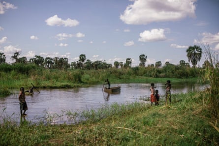 Children play on a flooded football pitch, including one child on a boat in the middle of the water.