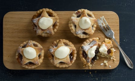 Five mince pies with cream on wooden serving tray. One pie half eaten.
