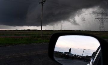 dark clouds in the sky and a person standing on a car reflected in the side mirror of another car