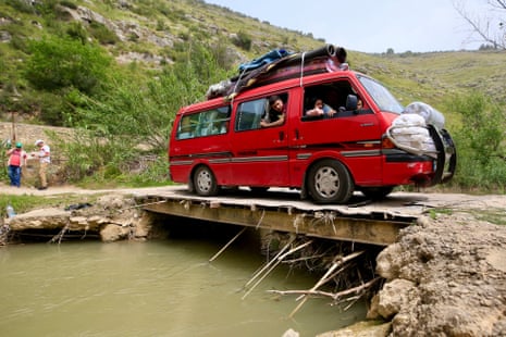 A red van drives across a makeshift bridge in lebanon, the occupants looking out of the windows cautiously.