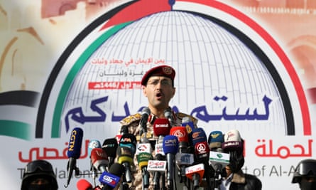 A Houthi spokesperson in uniform giving a press conference at a podium