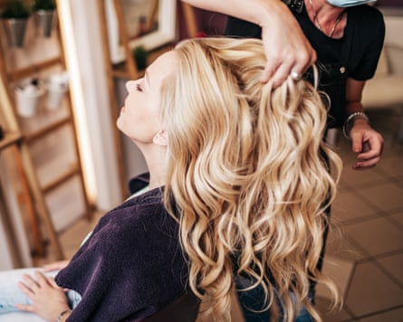 A blond woman getting her long hair curled and styled by a hairdresser