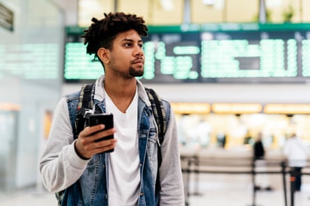 Young man inside the airport holding a mobile phone.young afro man holding a mobile phone looking at the departures of planes in an airport