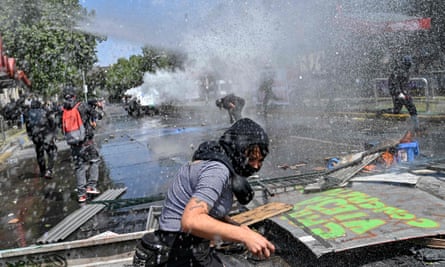 Demonstrators are sprayed with water cannons during clashes with riot police which erupted in a protest on the third anniversary of a social uprising against rising utility prices, in the surroundings of the Baquedano square in Santiago, on 18 October.