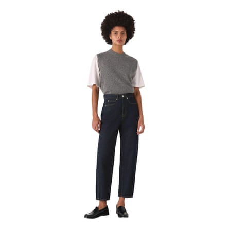 A model wears a pair of Whistles Dark Denim Authentic Barrel Leg Jeans, which are dark blue. They have a white T-shirt, grey vest and loafer style shoes.