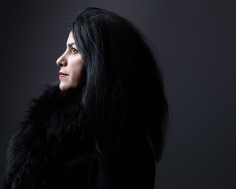 Marjane Satrapi in profile with long black hair and a fur collar against a dark background