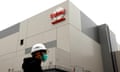 Person in hard hat and mask walking in front of a building bearing a TSMC logo in Taiwan