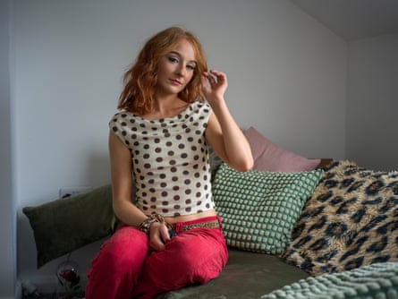 Young female successful a spotted apical and reddish trousers sitting connected a sofa, 1 manus twirling her hair.