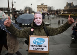 A protester wears a mask of Emmanuel Macron and a sign that reads “Pfizer salesman of the year” at the Paris rally.