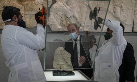 Two conservators at the  Acropolis Museum remove a glass case from a Parthenon fragment, on loan from the Antonino Salinas Regional Archaeological Museum of Palermo,
