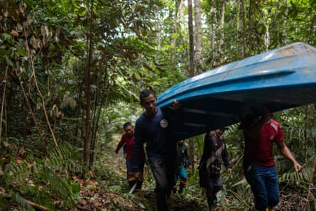 Five people carry a blue canoe on their shoulders through dense jungle