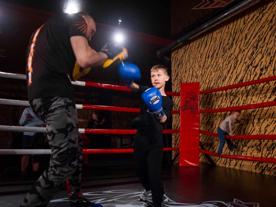 A young boy in boxing gloves throws punches at a trainer wearing pads on his hands