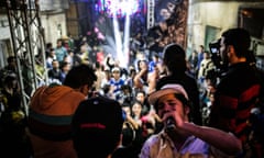 A man in a baseball cap drinks from a bottle with a crowd of people behind him at a street party in Cairo