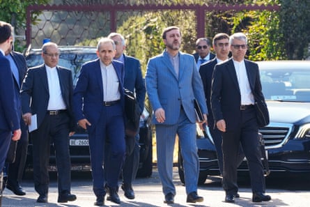 Members of the Iranian delegation wearing dark suits walk past parked cars