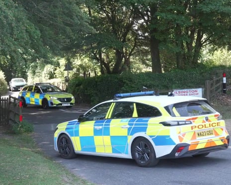Two police cars with checkered livery parked on a residential road near hedges and trees