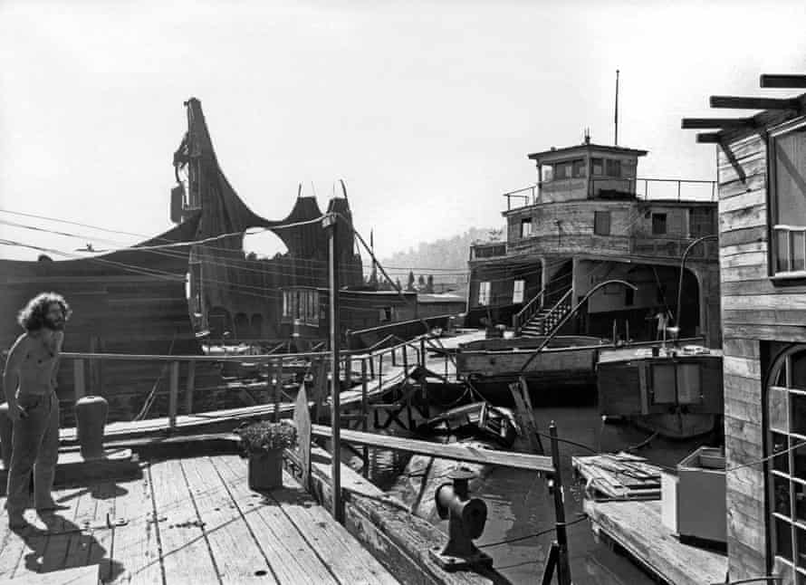 A man stands by the water among boats in a black and white image