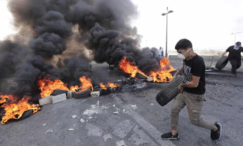 A protester places burning tyres on a road in Khalde, Lebanon