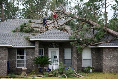 two people stand on house's roof to clear fallen tree