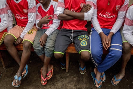 Boys whose faces we cannot see sit in a line of a bench wearing Arsenal jerseys.