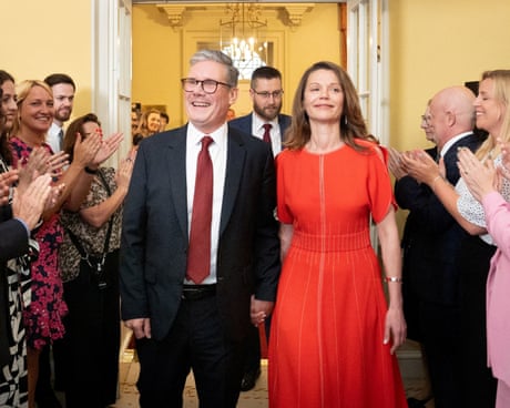 Keir Starmer and his wife smiling as people on either side of them applaud in 10 Downing Street