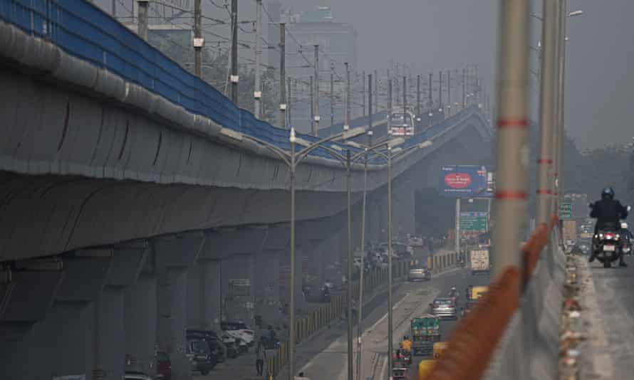 Commuters are driving along a road next to a subway line in New Delhi amid heavy smog