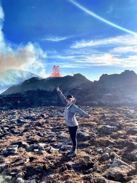 Kristín María Birgisdóttir stands with her arms in the air as a volcano spews lava in the background