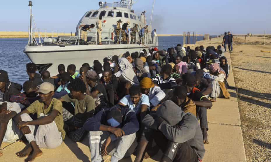 Rescued refugees seated next to a coastguard boat in Khoms, Libya, 1 October 2019