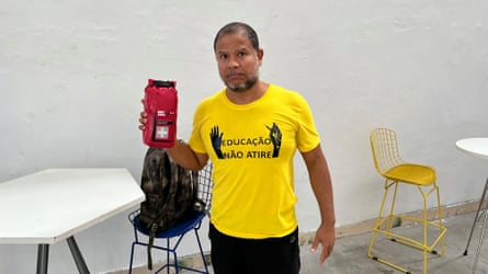 A man in a yellow shirt that reads ‘Education, don’t shoot’ holds a first-aid kit.