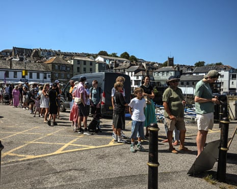 Members of the public queue for solar eclipse glasses at a stall on Custom House Quay in Falmouth, England.