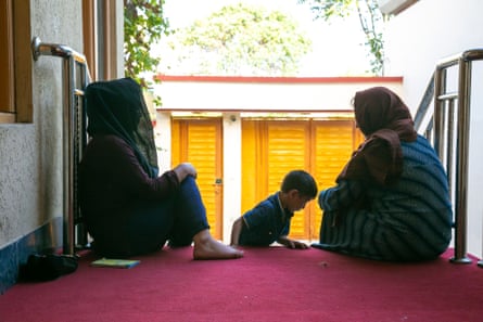 Two women sit on the steps of a house while a child plays nearby.