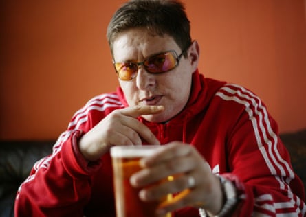 He wears a red Adidas hoodie and orange sunglasses and holds a beer