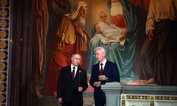 Vladimir Putin and Moscow’s mayor, Sergei Sobyanin, hold lit tapers in front of a large religious painting