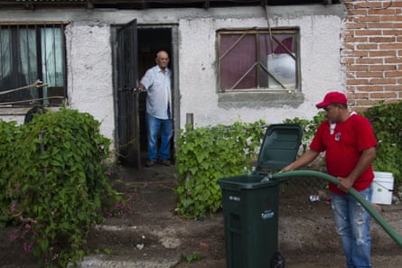 A man pouring water into a trash can.