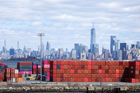 A high stack of red shipping containers with the city skyline in the background
