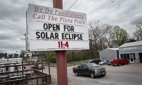 Under a cloudy sky, a signboard above a street says "We do fundraisers / Call the pizza pros / Open for solar eclipse 11-4".