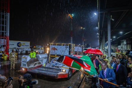 A crowd of people, some waving the Kenyan flag, at the airport.