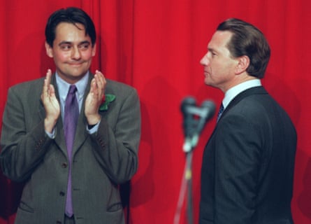 Michael Portillo standing in profile against a red background after losing his seat to Labour’s Stephen Twigg, who is standing smiling and clapping