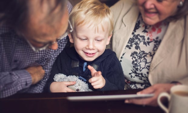 Young boy and grandparents look at a tablet. Picture posed by models.