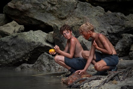 Two boys kneel beside a stream, stripped down to their school shorts