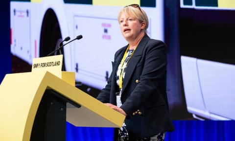 Shona Robison stands behind a yellow SNP lectern