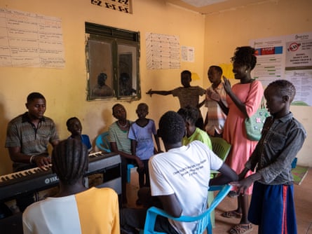 A man sits at a keyboard with children and other adults gathered around
