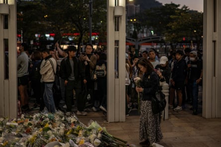 Woman holds flower by memorial with line of people waiting behind
